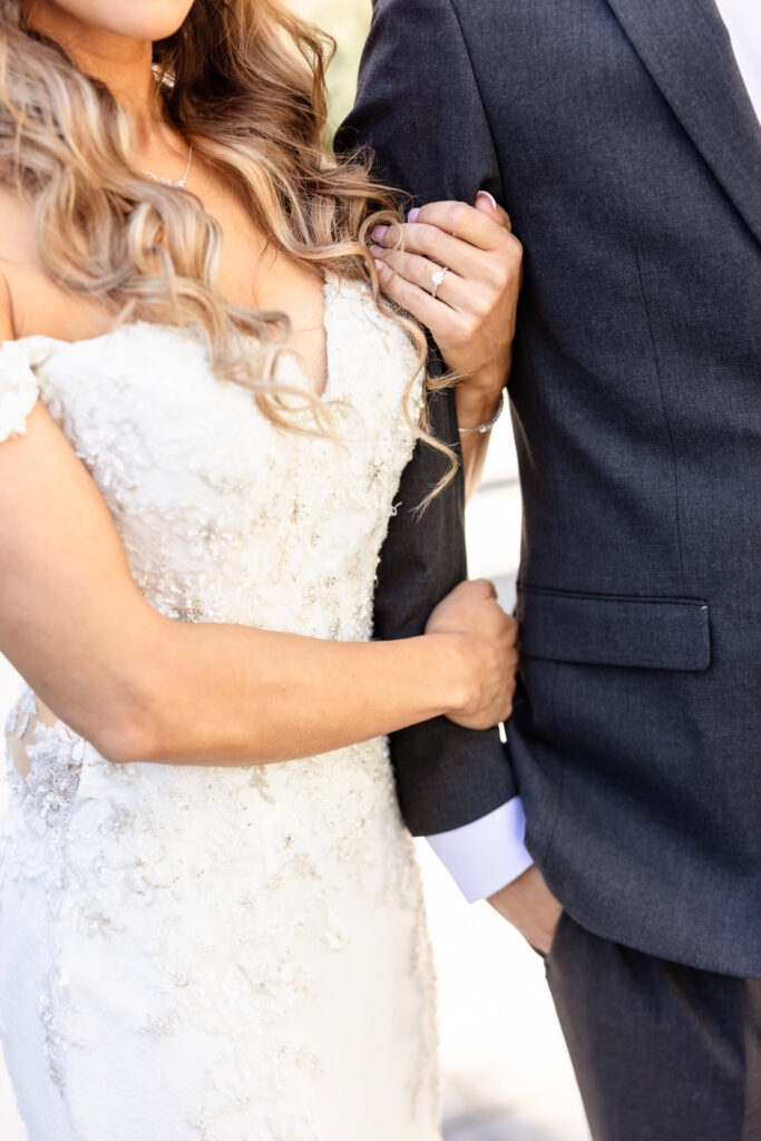 Close-up of bride and groom holding arms, showcasing intimate connection and gown details.