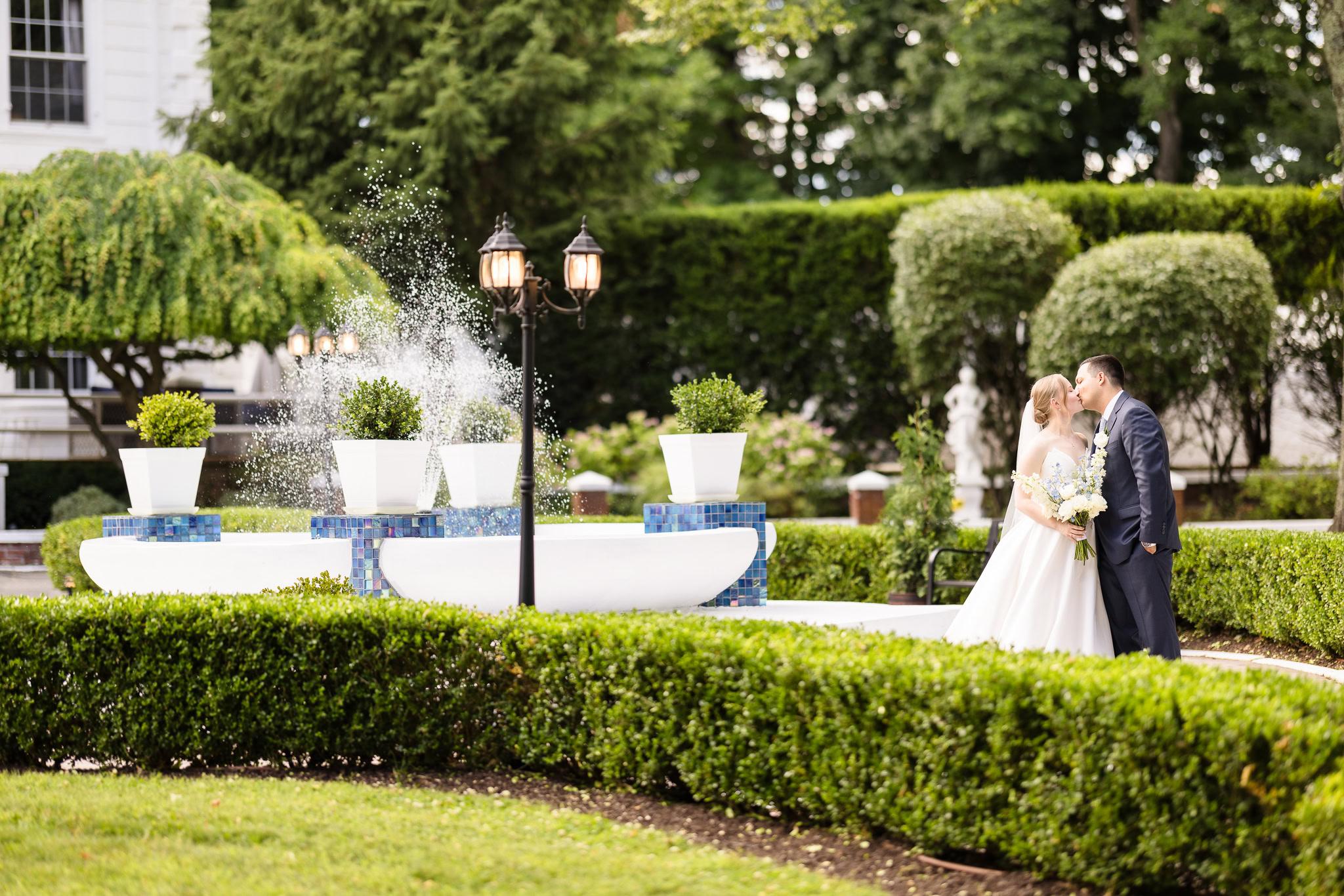 Bride and groom sharing a kiss beside the elegant fountain and manicured gardens at The Briarcliff Manor in Westchester.