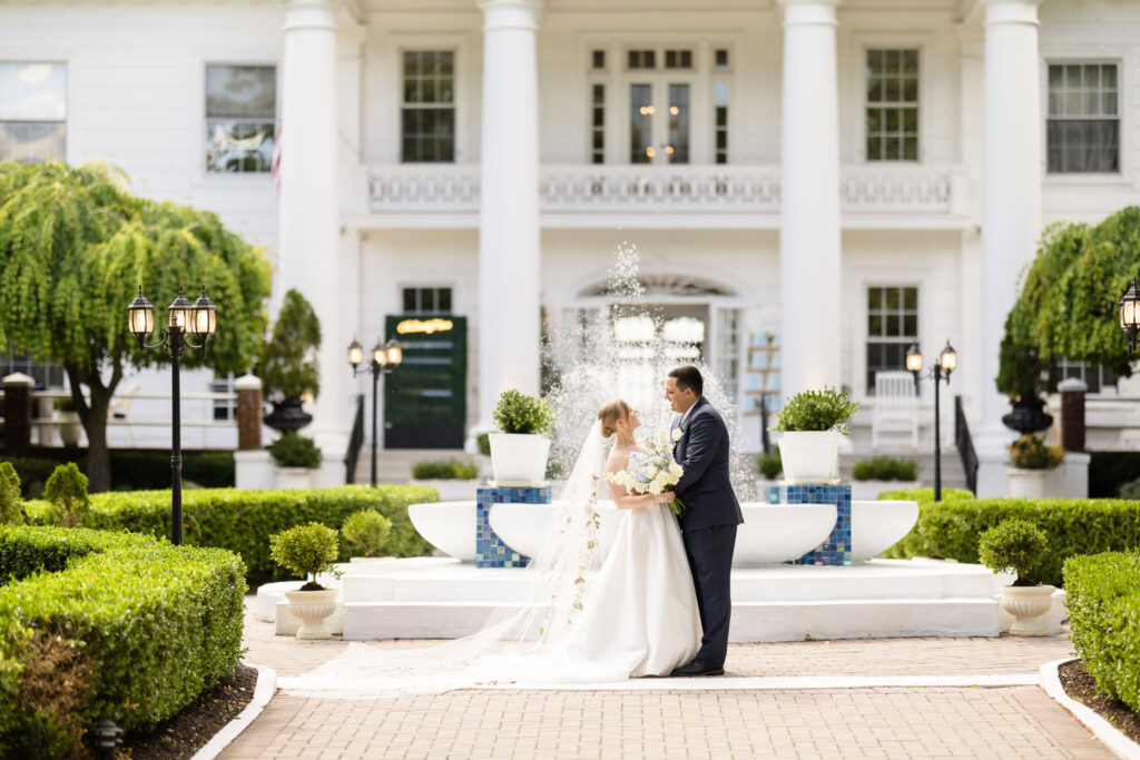 Bride and groom embracing in front of the historic mansion and fountain at The Briarcliff Manor wedding venue.
