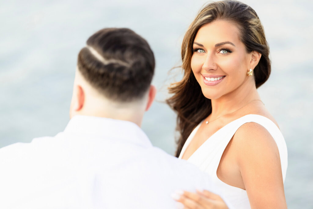 Christine smiling warmly toward the camera with Matt turned slightly away, the harbor softly blurred in the background.
