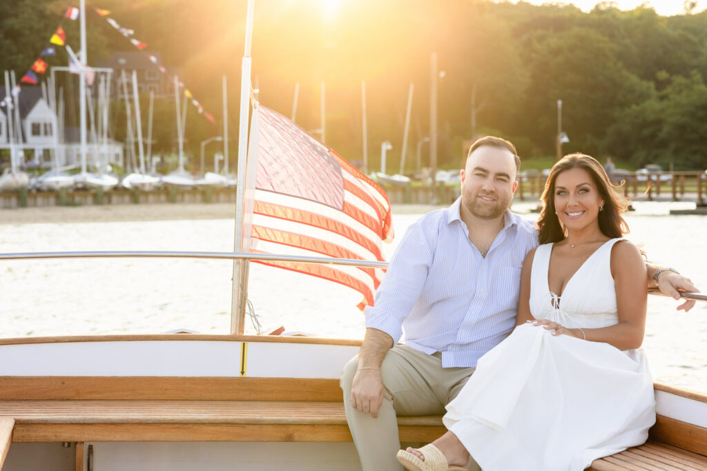 Couple seated at the stern of a launch boat with an American flag, sunlight streaming over the water.