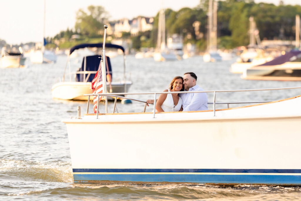 Couple riding through Centerport Harbor on a small boat, smiling as the shoreline passes behind them.