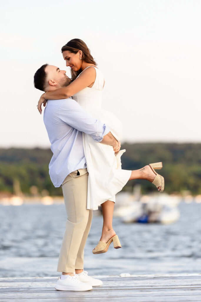 Matt lifting Christine in his arms along the dock, both smiling against the backdrop of the water.