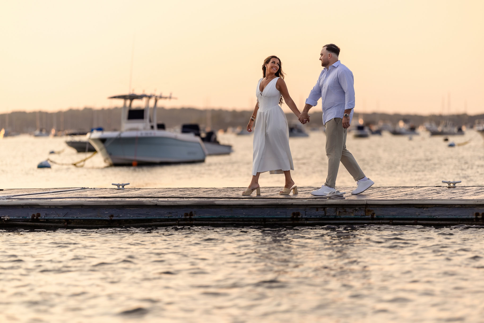 Couple walking along the dock at sunset, boats moored in the background.