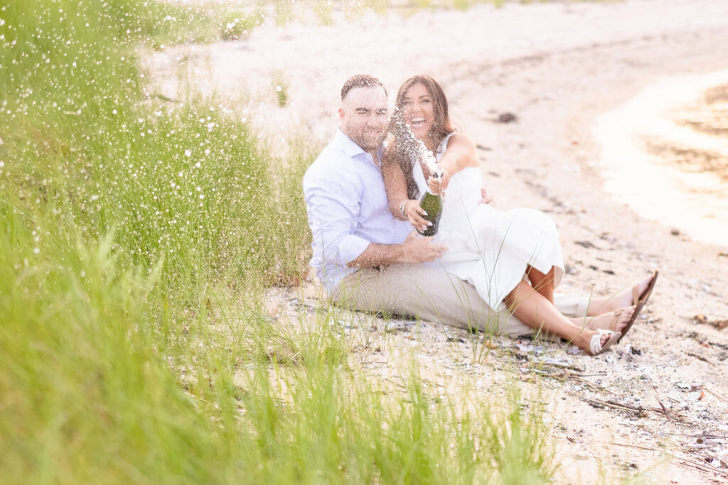 Christine and Matt seated together on the sand, leaning close with the shoreline behind them.