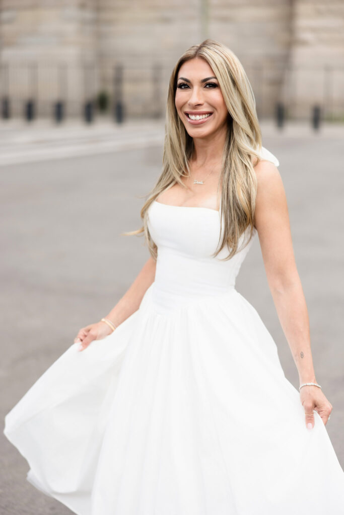 Smiling woman in a white dress holding her skirt during a DUMBO engagement session.