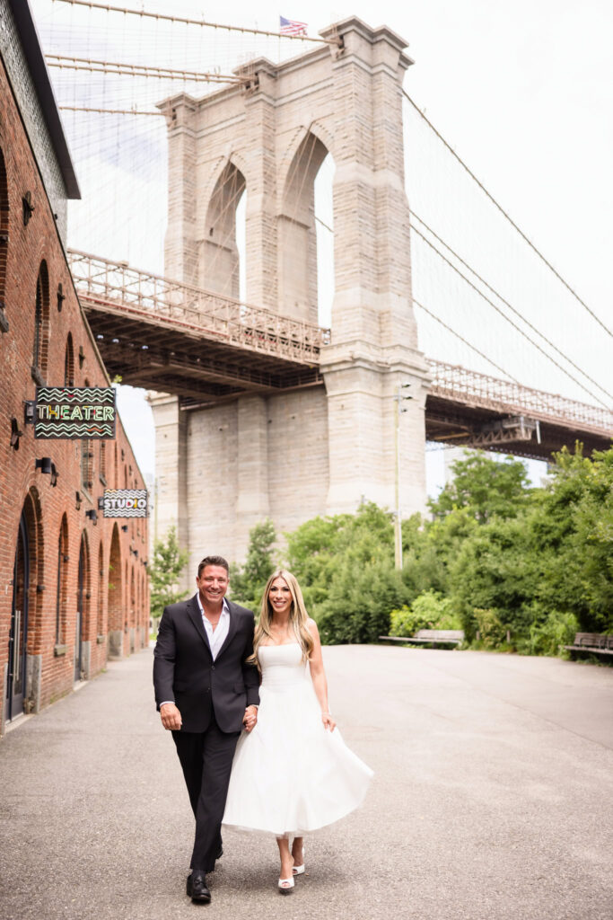 Couple walking hand in hand near St. Ann’s Warehouse with the Brooklyn Bridge in the background.