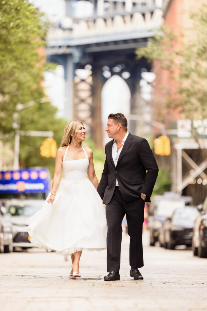 Couple walking on cobblestone street in DUMBO with the Manhattan Bridge in the background.