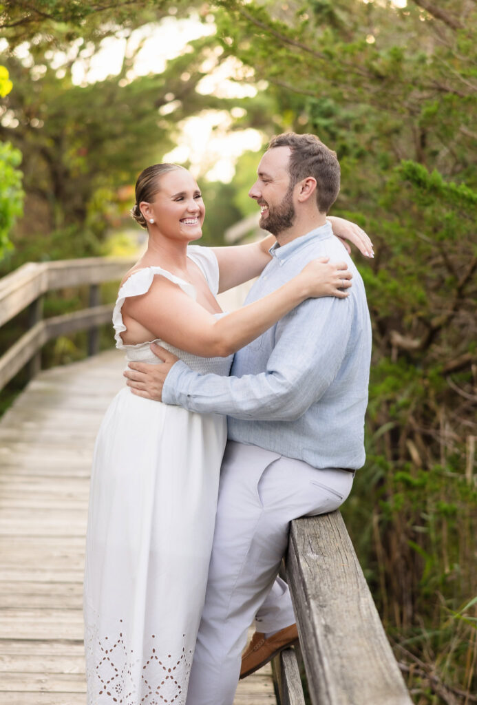 Couple smiling and embracing on a wooden boardwalk at Fire Island during their engagement session.