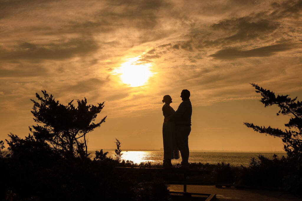 Silhouette of a couple standing together at Fire Island during sunset with golden light over the water.