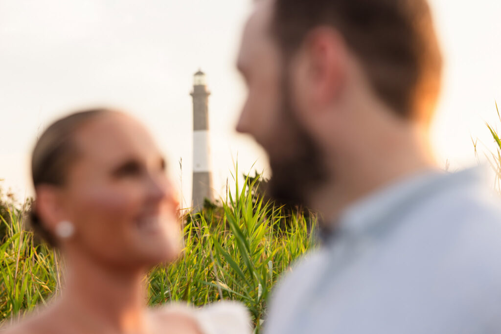 Out-of-focus couple with Fire Island Lighthouse in sharp focus behind them at sunset.