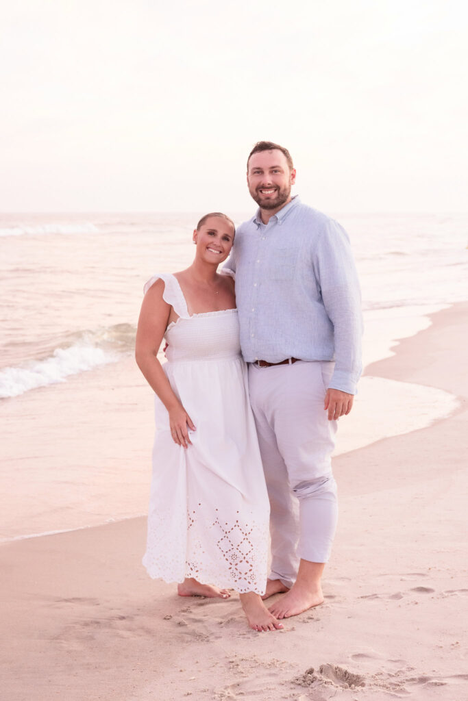 Couple standing barefoot on the sandy beach at Fire Island with soft pastel evening light.