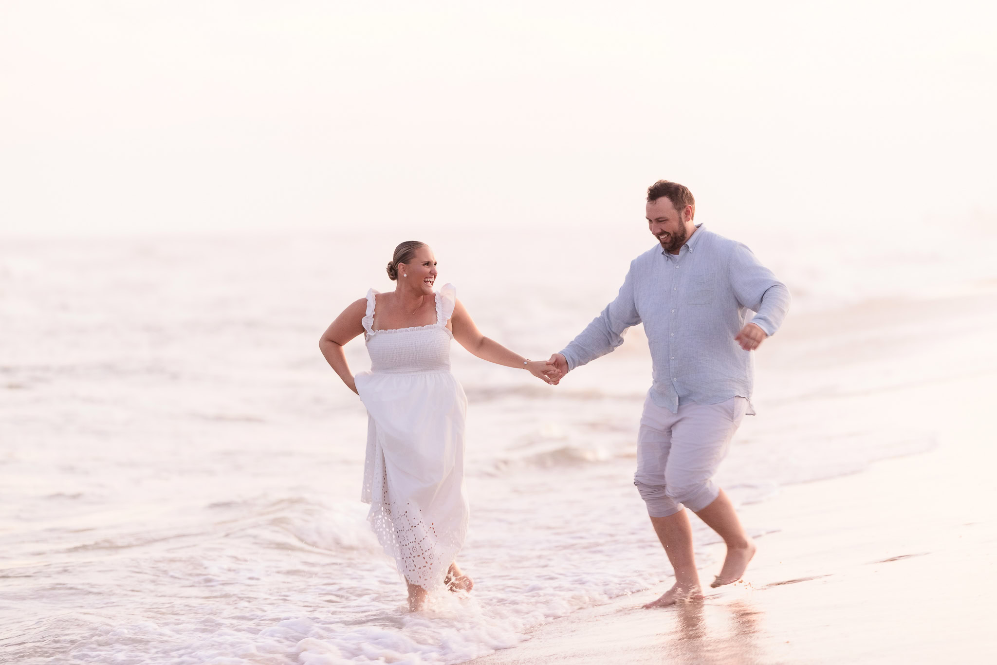 Couple holding hands and laughing while walking through the waves at Fire Island beach.