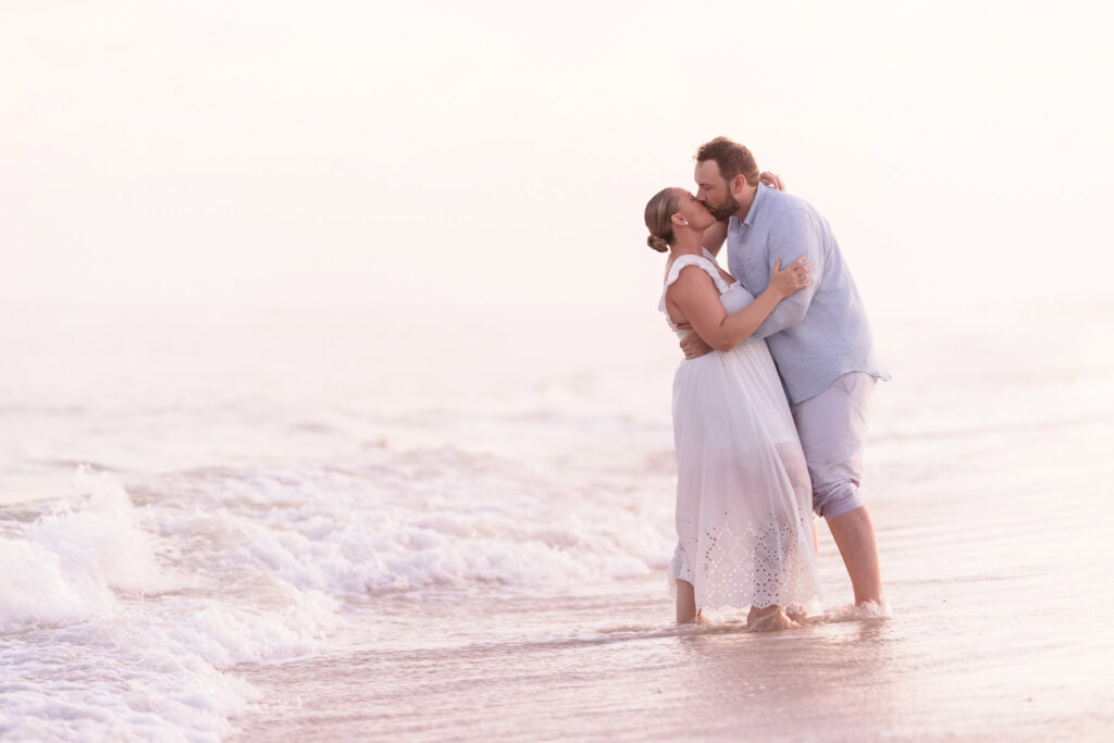 Couple kissing in the ocean waves at Fire Island, standing barefoot in the water during sunset.