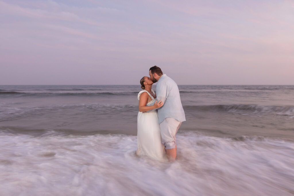Couple kissing in the surf at Fire Island as waves rush around them during their engagement session.