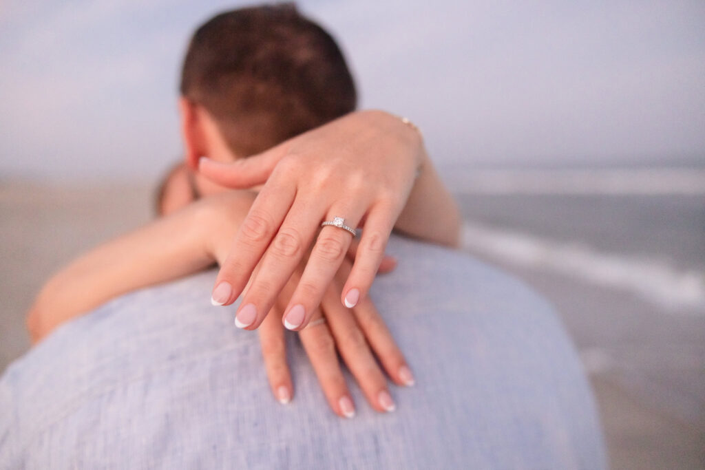 Close-up of an engagement ring as the bride rests her hand on her partner’s shoulder at Fire Island beach.