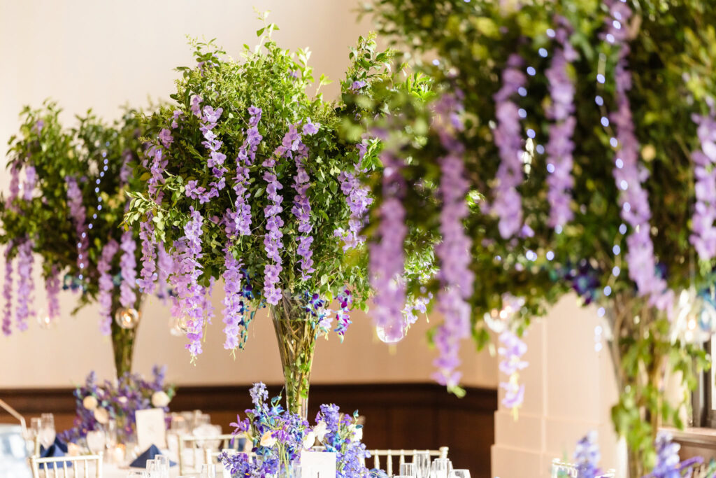 Reception table centerpiece featuring cascading wisteria in purple tones, styled with greenery and soft candles.