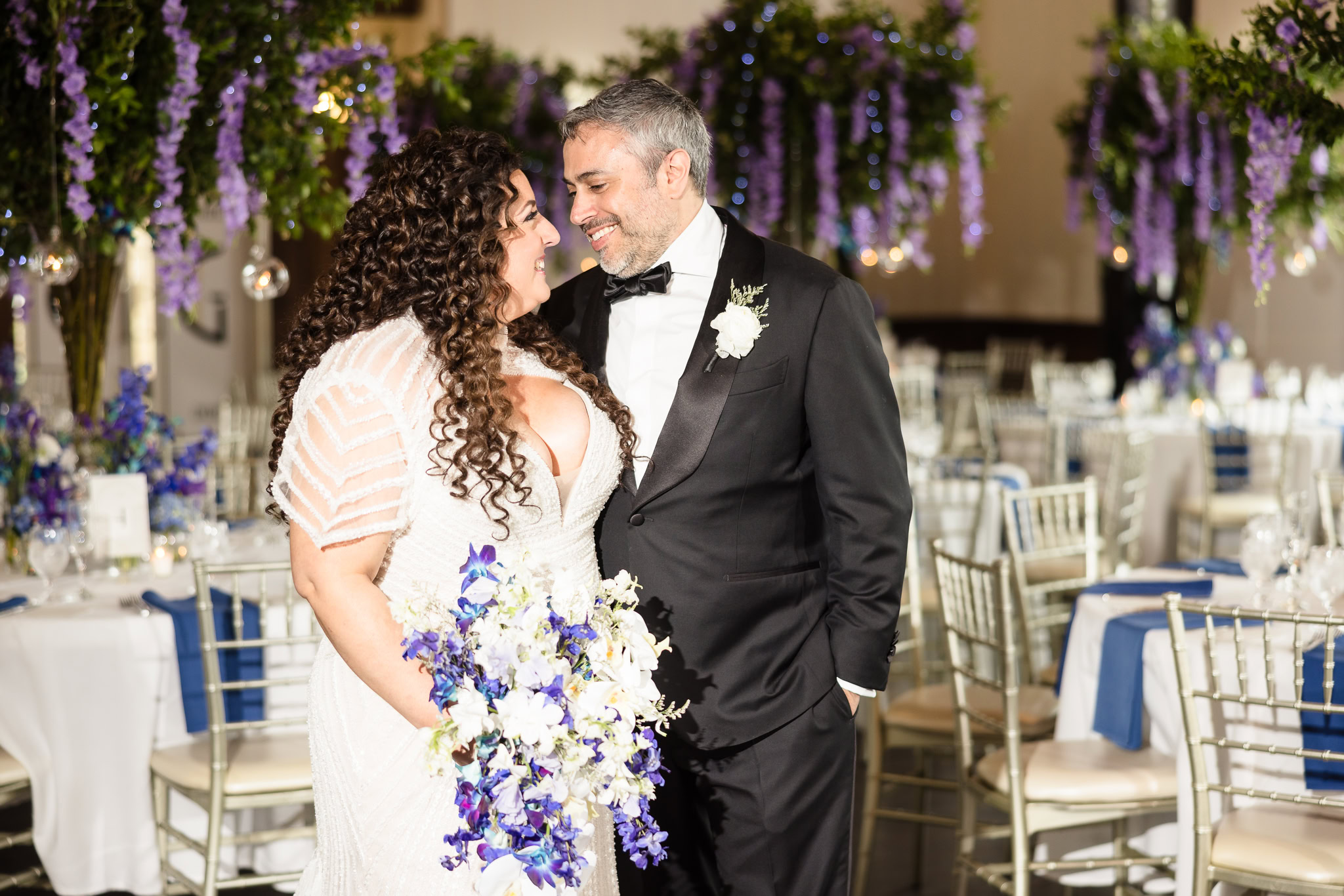 Bride and groom dancing together at their reception, surrounded by floral tablescapes and soft lighting.