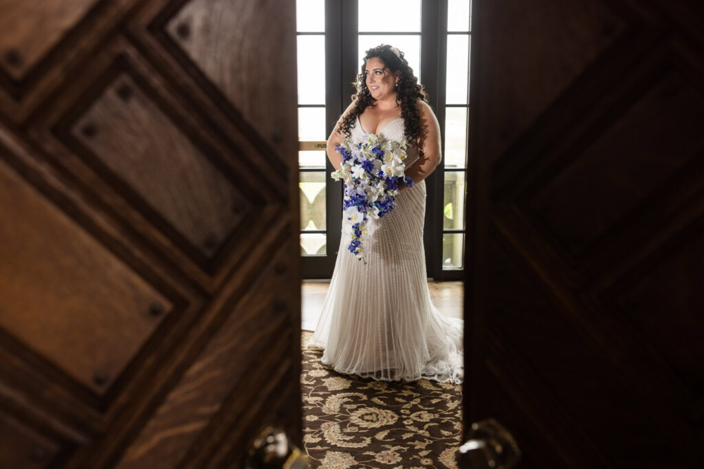Bride standing in the doorway at Gatsby on the Ocean, holding her bouquet and looking serene before the ceremony.