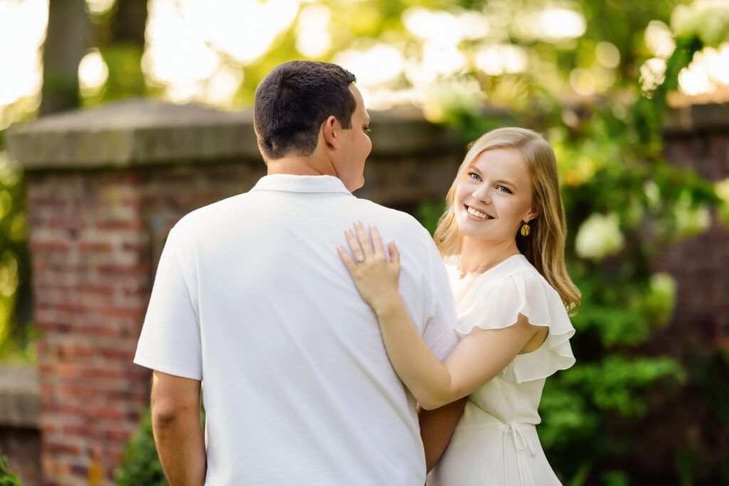 Groom-to-be embraces his fiancée during a golden summer evening at Greenwich Point Park, Long Island Sound in the background.