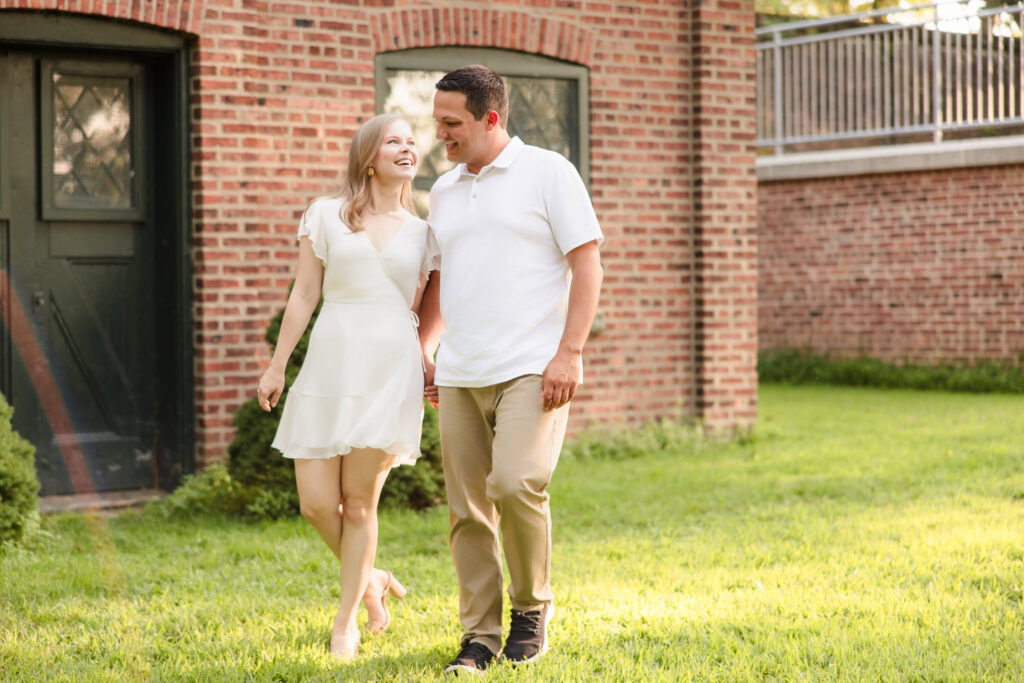 Couple walking hand in hand along a brick path, smiling warmly at each other in Greenwich Point Park.
