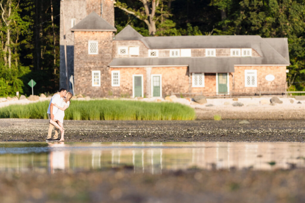 Couple walking along the shoreline with the historic stone building of Greenwich Point Park in the background.
