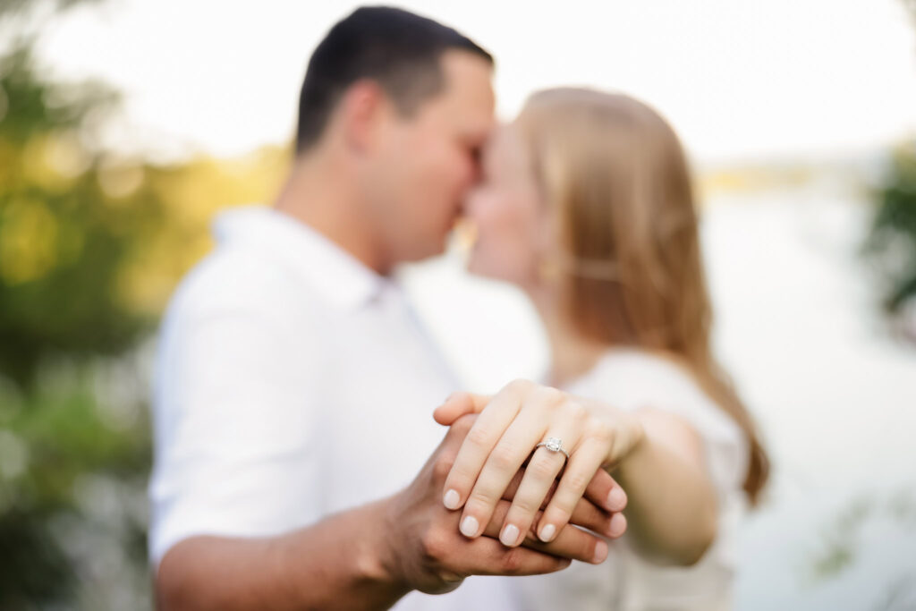 Couple holding hands with blurred background, focusing on engagement ring at Greenwich Point Park.