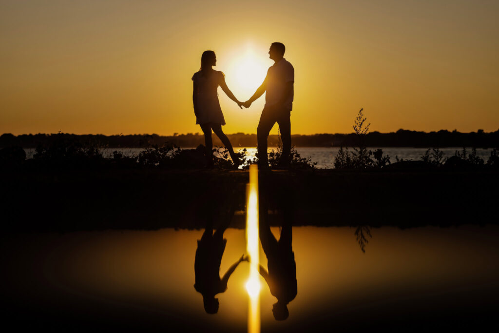 Silhouette of couple holding hands against a glowing orange sunset at Greenwich Point Park shoreline.
