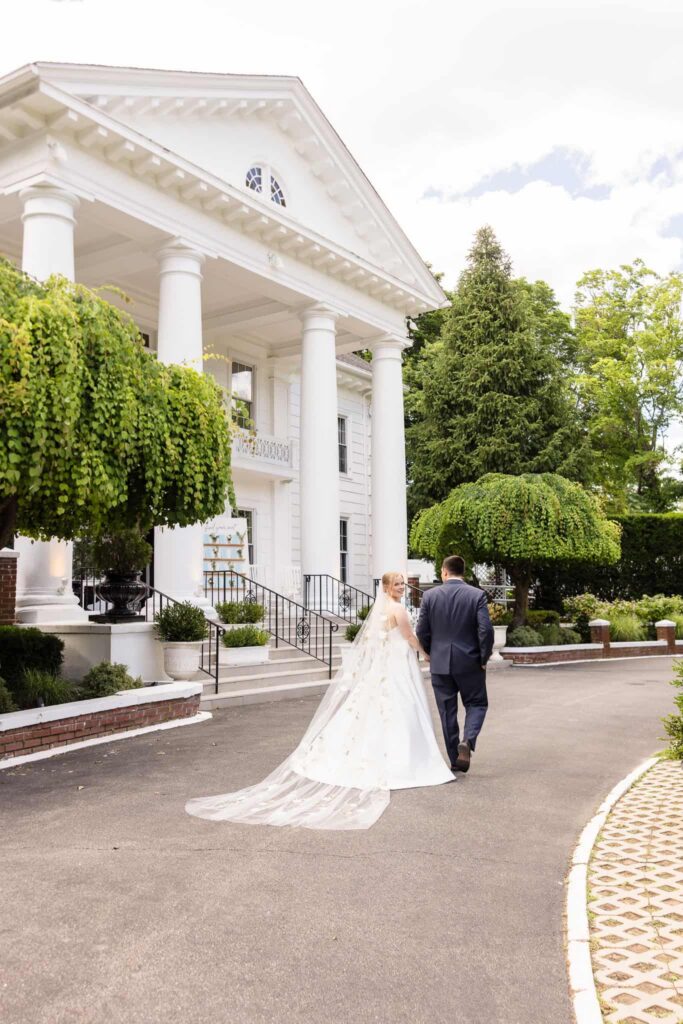 Bride and groom walking hand in hand outside the elegant entrance of Watermill Caterers after their ceremony.