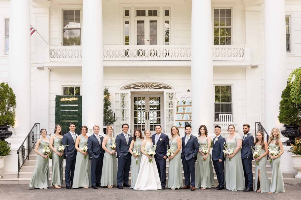 Wedding party posing in front of the elegant white mansion entrance at Watermill Caterers in Smithtown.