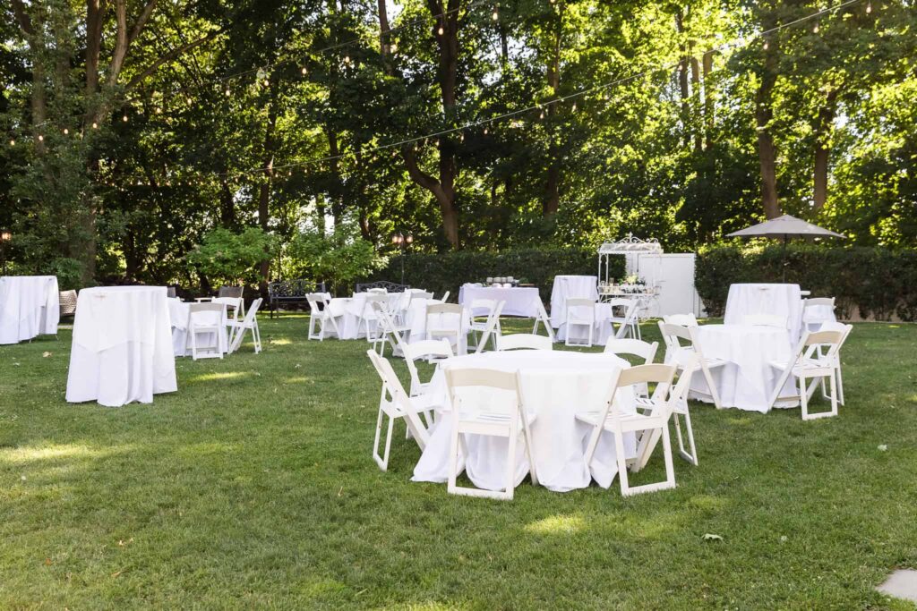 Outdoor cocktail hour setup with white tables and string lights on the lawn at Watermill Caterers.