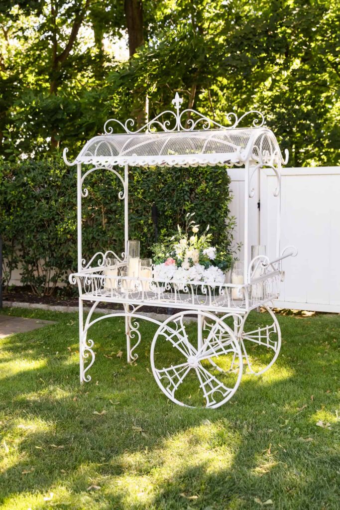 Decorative white vintage cart displaying wedding florals and candles for an outdoor ceremony at Watermill Caterers.
