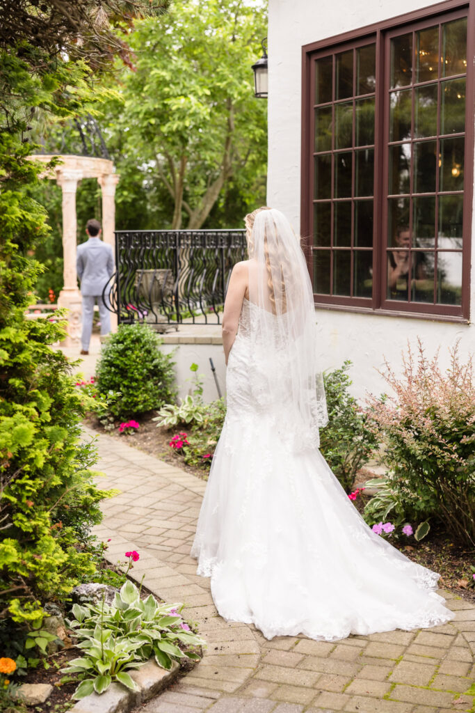 Bride walking alone along a cobblestone path at Riviera Waterfront Mansion, veil flowing as she approaches her first look.