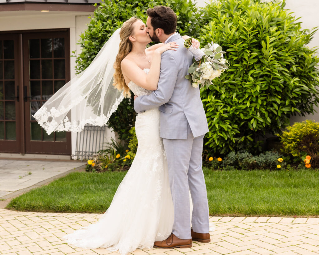 Bride and groom sharing a joyful kiss outdoors, veil floating in the breeze as they celebrate their marriage.