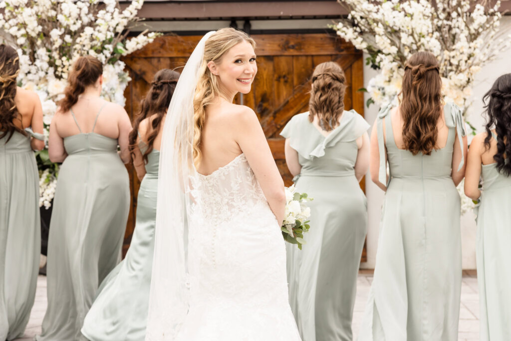 Bride turning to smile at her bridesmaids as they walk towards the ceremony space, excitement building.