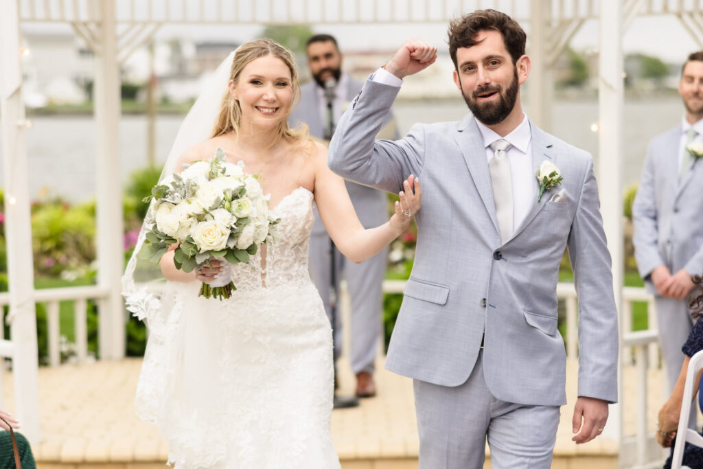 Newlyweds walking up the aisle hand in hand, smiles wide as guests cheer around them.