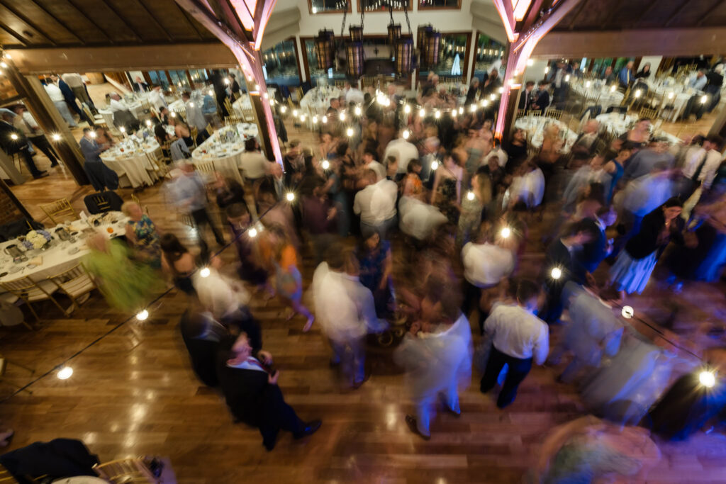Blurred, lively scene of guests dancing together on the wooden dance floor during the reception celebration.