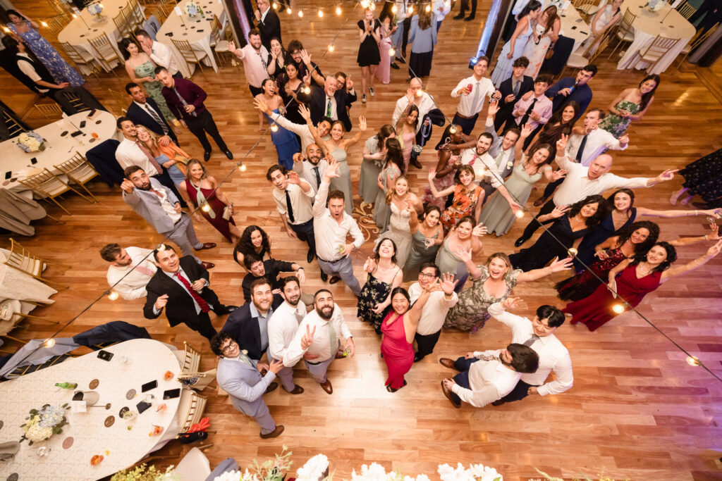 Overhead view of all the wedding guests gathered on the dance floor, smiling and waving towards the camera.