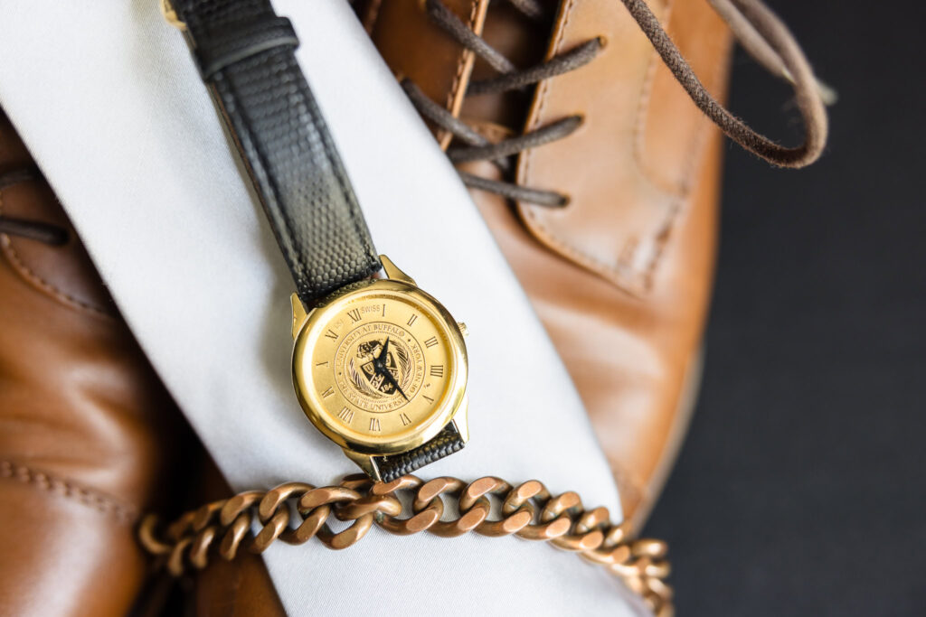 Groom’s brown leather shoes with a gold watch and black strap laid neatly, styled for a classic groom detail shot.