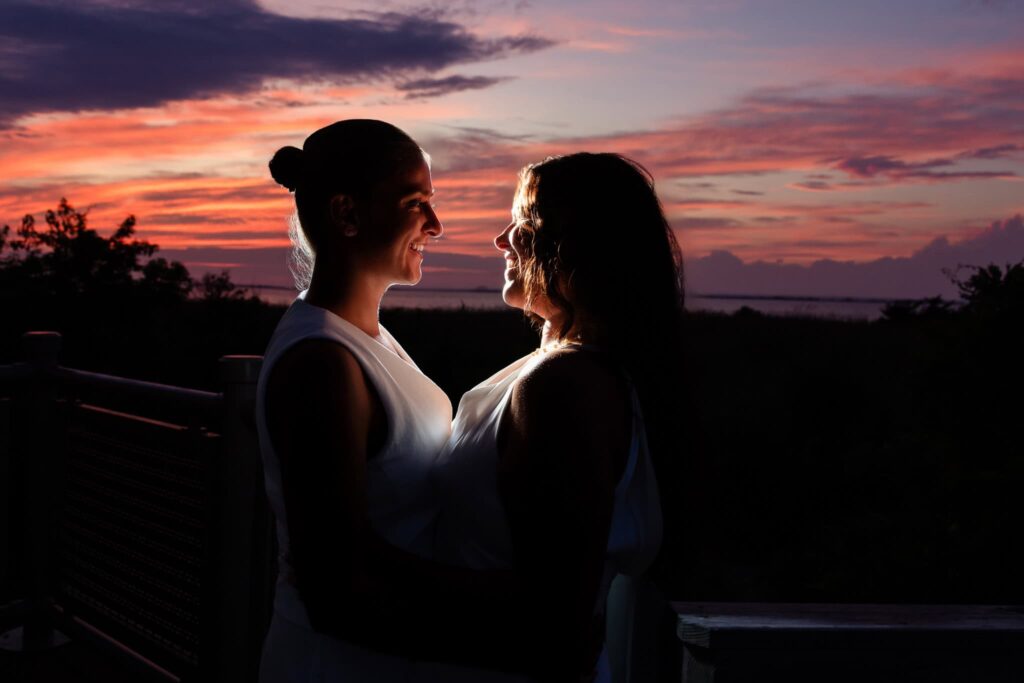 Couple standing face to face, softly illuminated as twilight falls, with hints of sunset glow in the background.