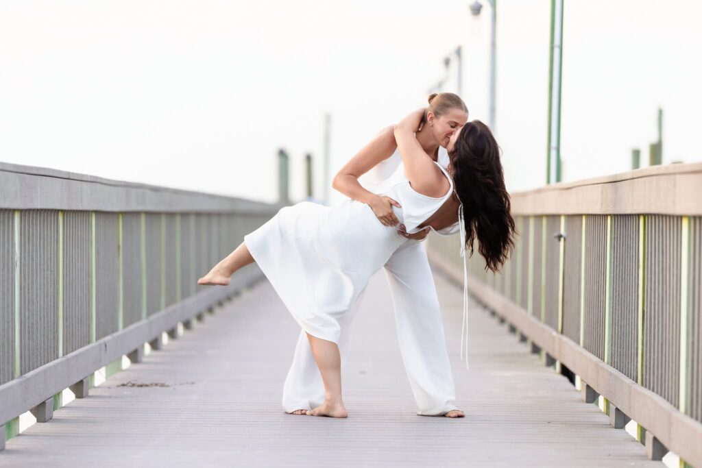 Couple embracing and dancing playfully on a wooden boardwalk, soft summer light wrapping around them in a carefree moment.
