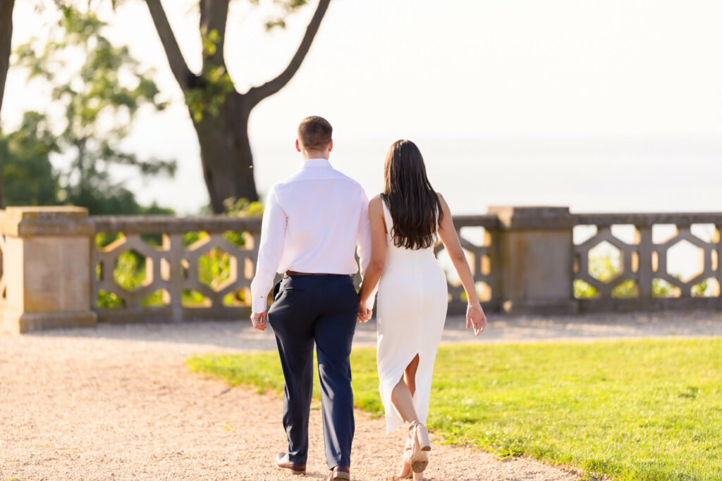 Couple walking hand in hand toward a stone terrace at Sands Point Preserve during golden hour.