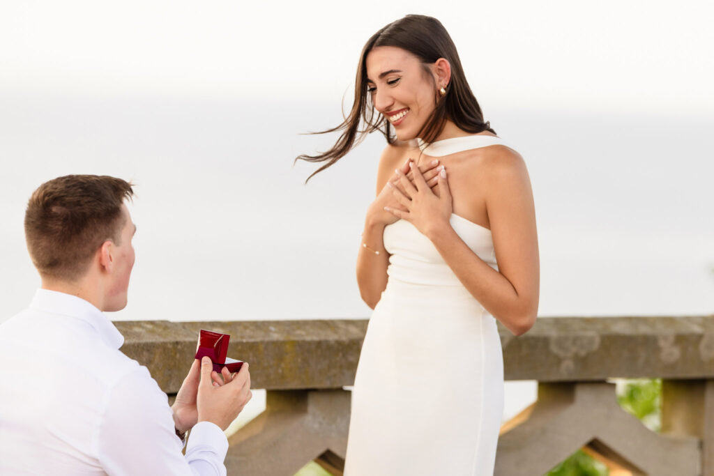 Woman smiling with hands over her heart during a surprise proposal in Long Island.