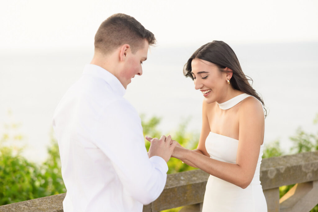 Man placing an engagement ring on his partner’s finger during a sunset proposal on Long Island.