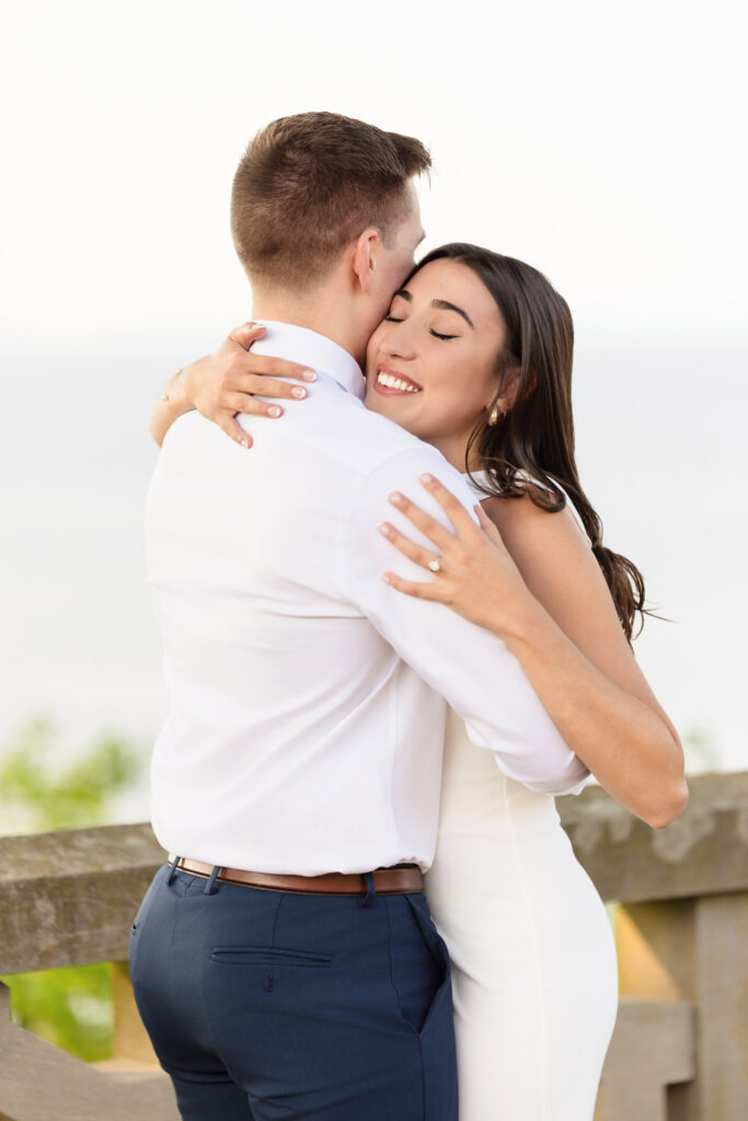 Couple embracing after their proposal with her engagement ring visible and eyes closed in joy.