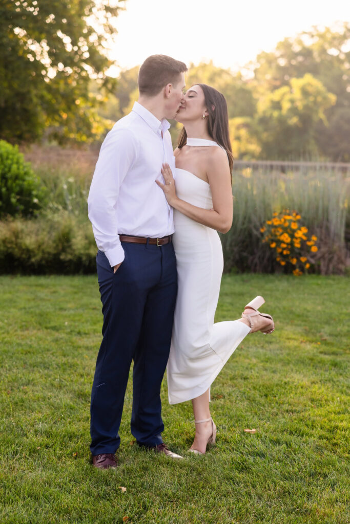 Couple kissing on the lawn with wildflowers and golden hour light in the background.