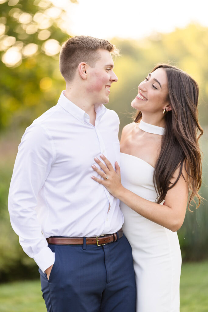 Couple smiling at each other closely during their post-proposal session in a sunlit garden.