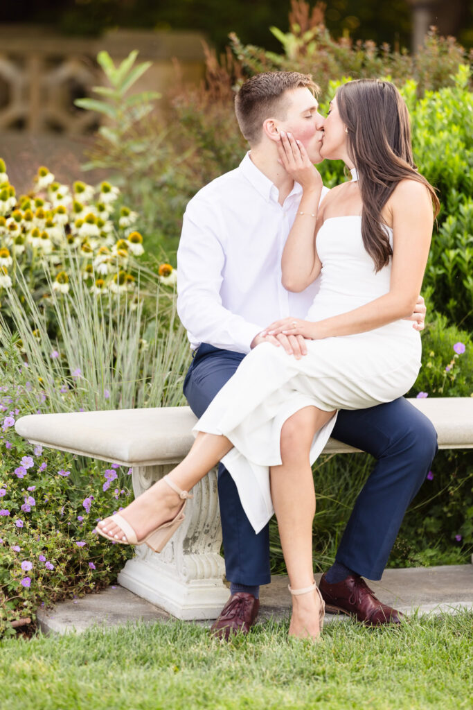 Couple sharing a kiss on a garden bench surrounded by late-summer blooms at Sands Point Preserve.