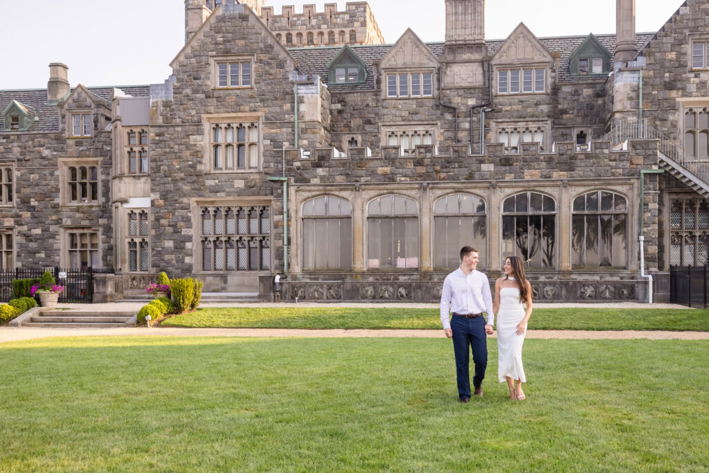 Couple walking hand in hand across the lawn in front of the historic mansion at Sands Point Preserve.