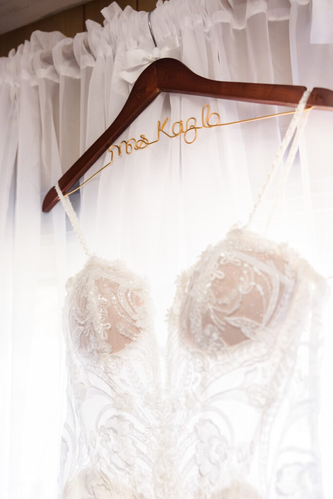 Close-up of lace wedding dress with beaded details hanging on custom hanger before the Camp Pa-Qua-Tuck wedding.